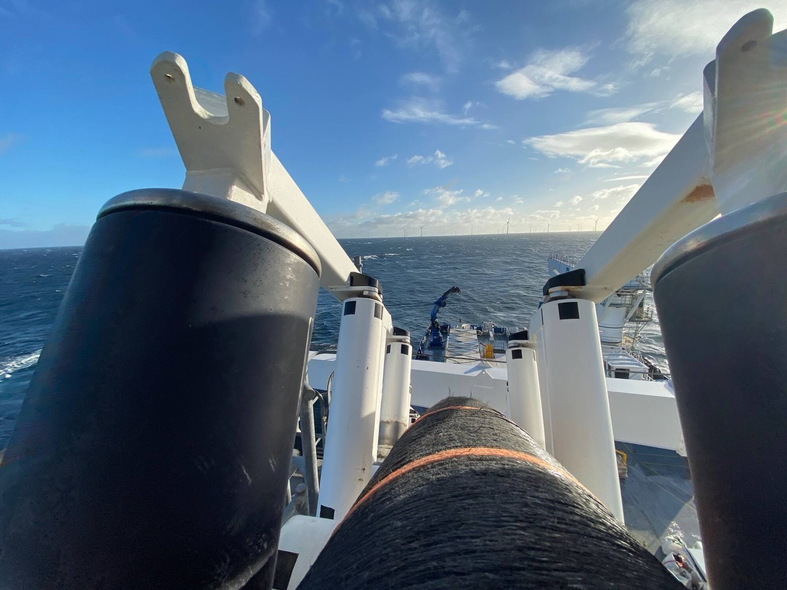 Subsea cable running through the deck tensioner during a cable-lay campaign, offshore wind farm on the horizon